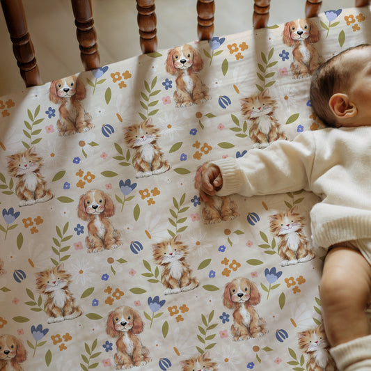 Baby lying on a crib with a patterned sheet featuring dogs, cats and flowers