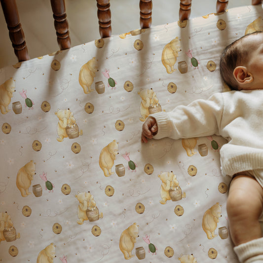 Baby lying on a crib with a patterned sheet featuring winnie the pooh and piglet.
