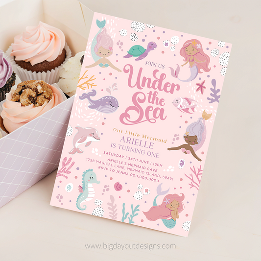 Invitation card with mermaid theme and cupcakes on a white surface