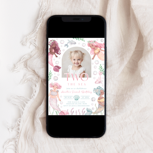 Phone displaying a birthday invitation with mermaid theme on a white fabric background