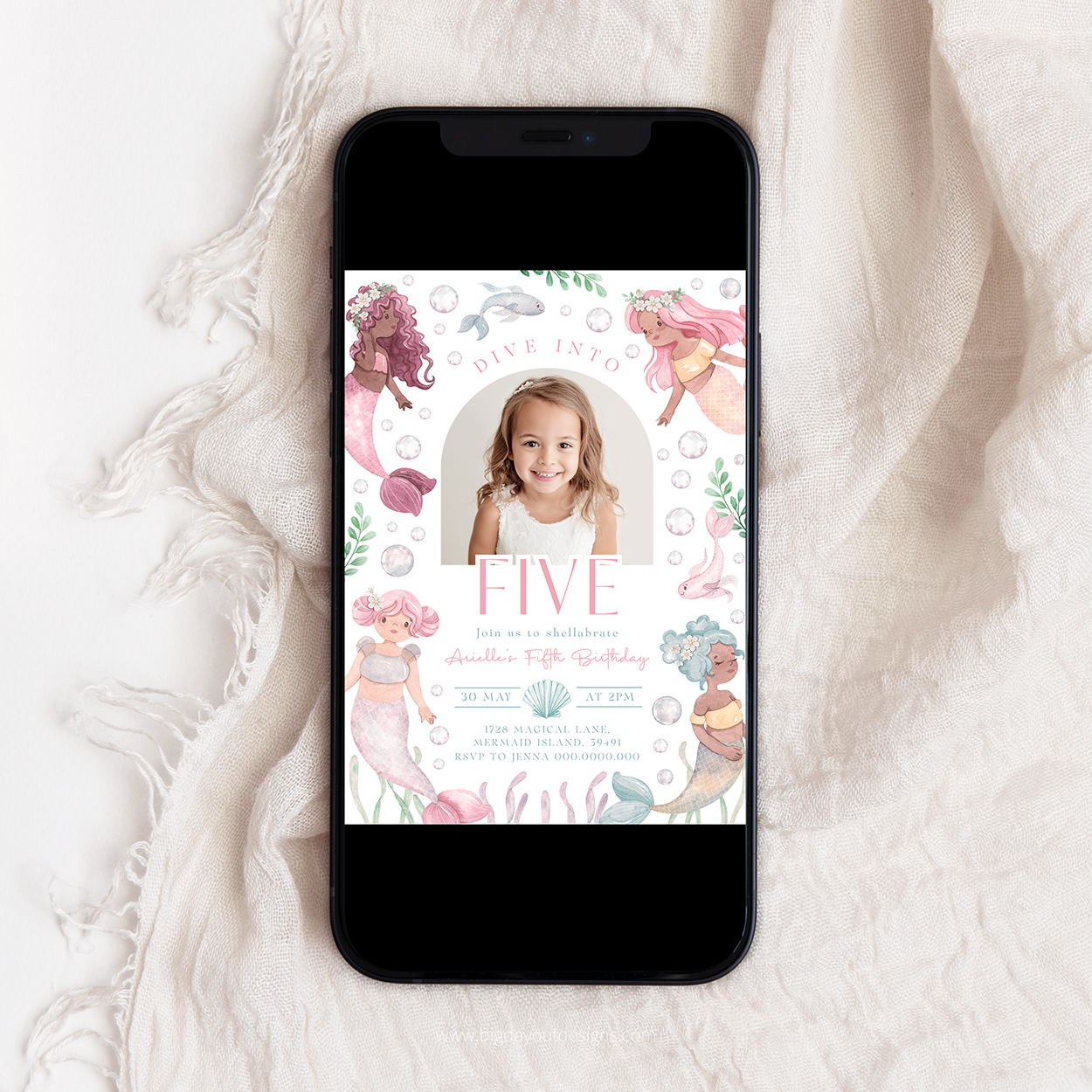 Phone displaying a birthday invitation with mermaid theme on a white fabric background
