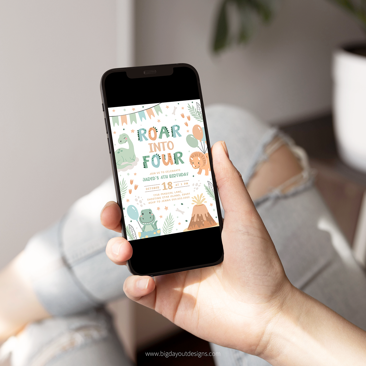 Hand holding a smartphone with a dinosaur-themed birthday invitation on the screen, sitting on a couch.