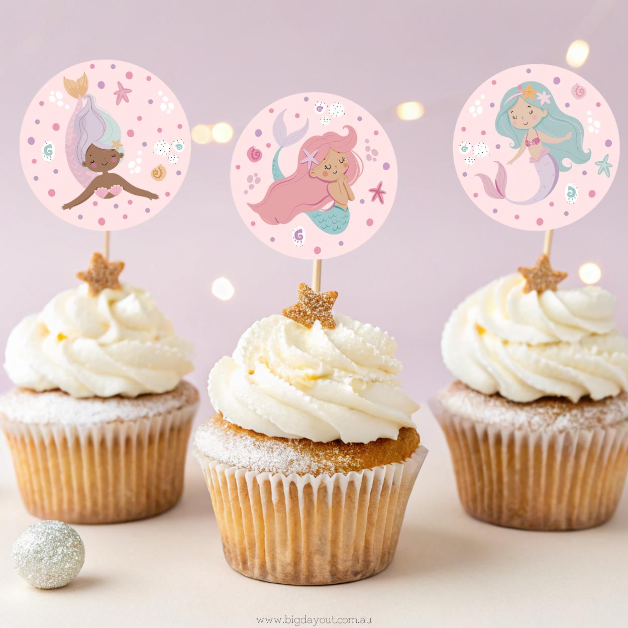 Three Mermaid Birthday Themed cupcakes with white frosting and decorative toppers on a light pink background