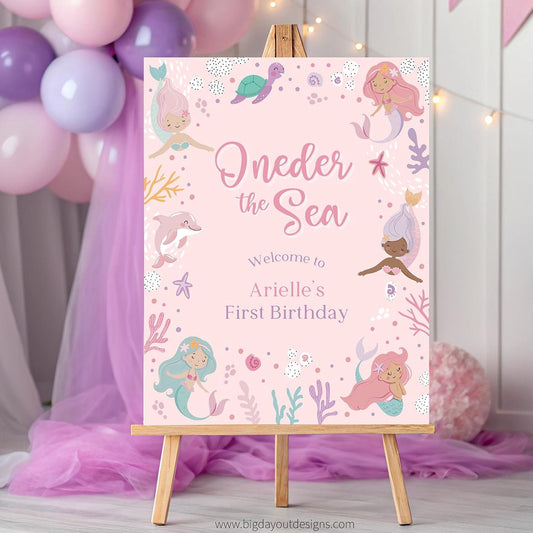 Pink birthday party sign with mermaid theme on a wooden easel, surrounded by balloons and decorations.