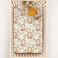 Crib with a floral cottagecore cat patterned sheet on a white background