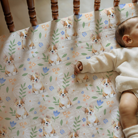 Baby playing with a crib sheet featuring corgi dogs and floral patterns.