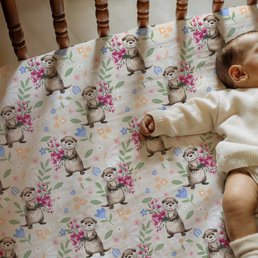 Baby interacting with a patterned blanket featuring otters and flowers.