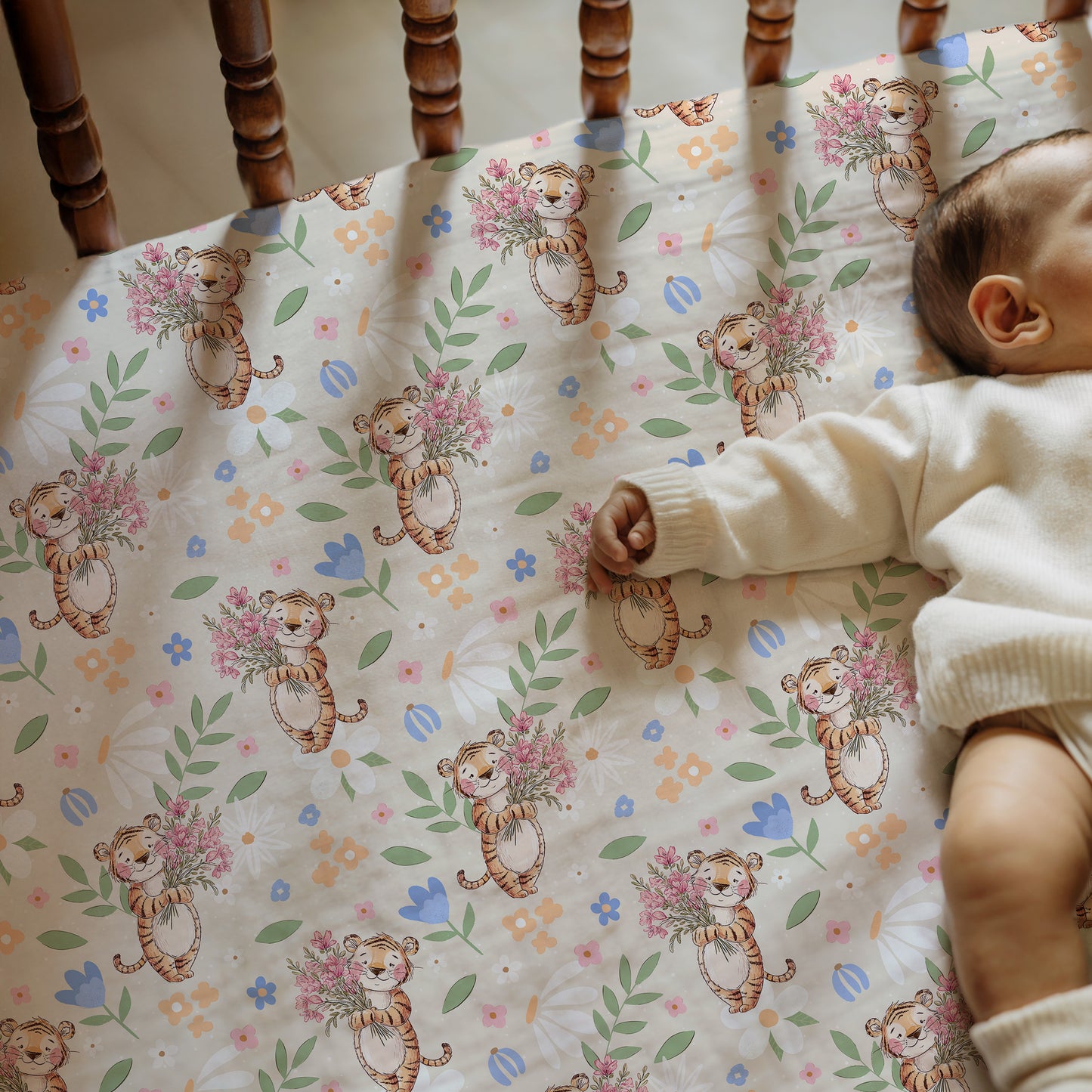Baby lying on a crib sheet with tiger and flower pattern, next to wooden crib bars.