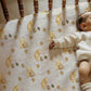 Baby lying on a crib with a patterned sheet featuring winnie the pooh and piglet.
