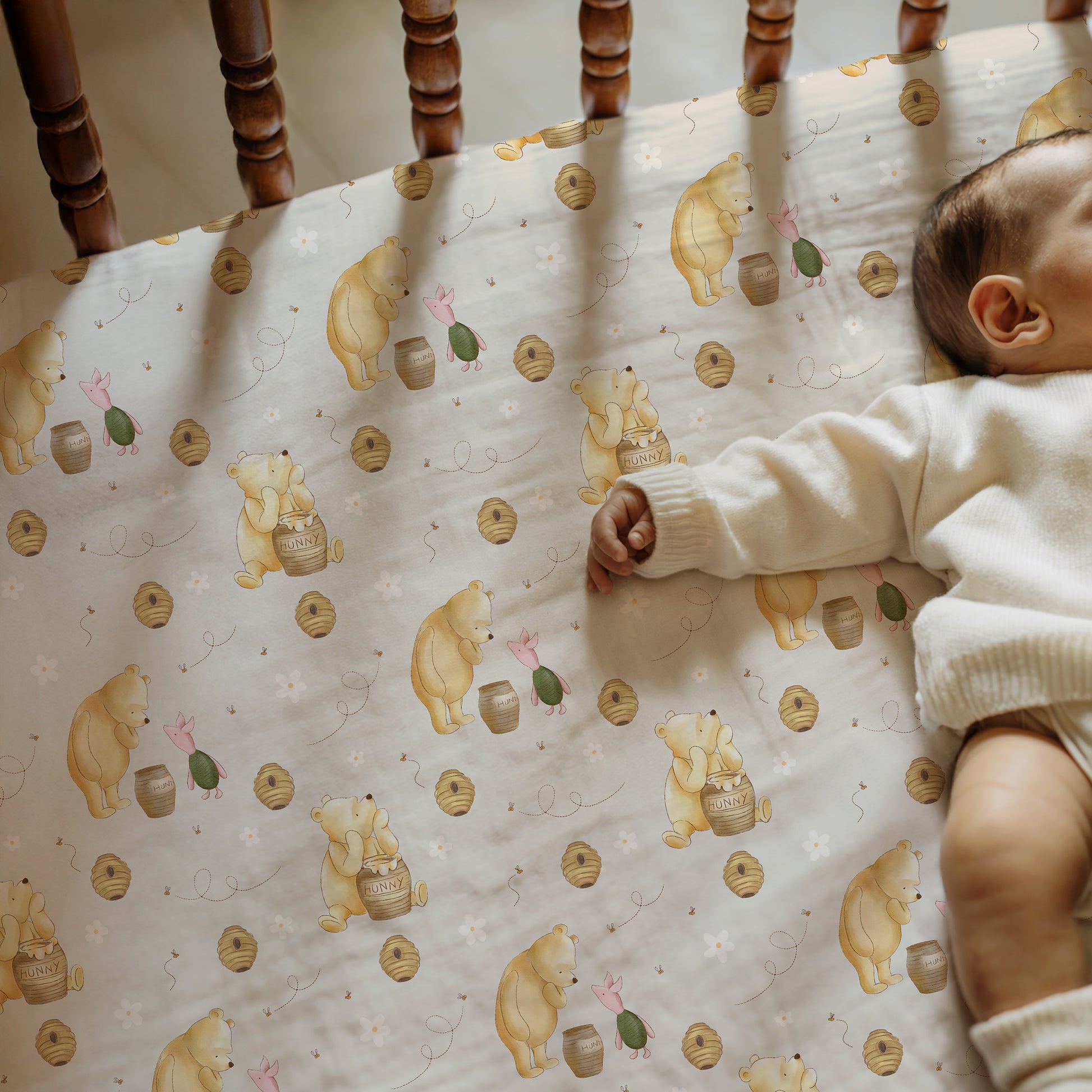 Baby lying on a crib with a patterned sheet featuring winnie the pooh and piglet.