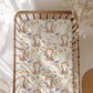 Crib with a patterned sheet featuring cartoon cats and flowers.
