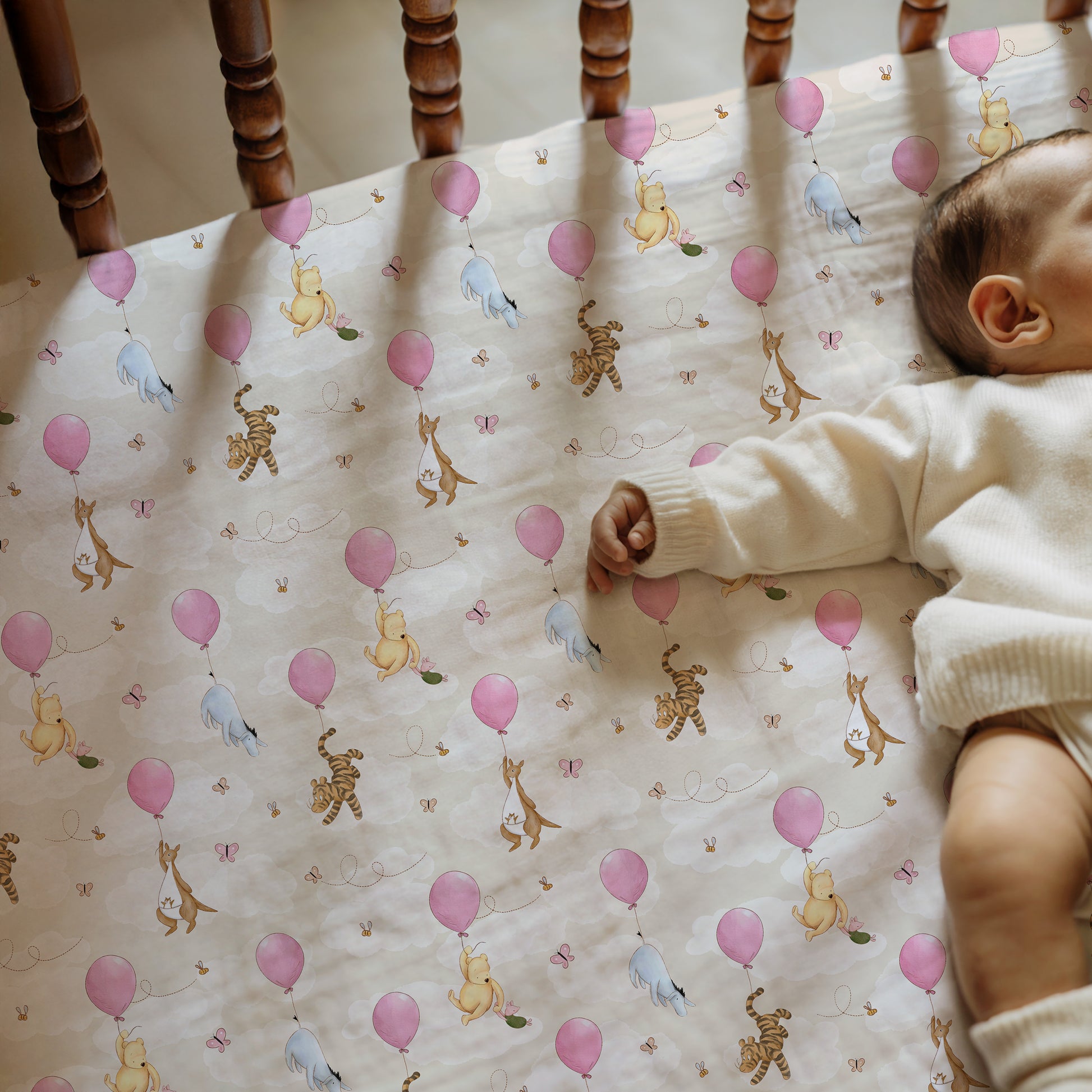 Baby lying on a crib with a patterned sheet featuring classic winnie the pooh and friends hanging onto balloons in the clouds