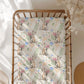 Baby crib with a sheet featuring cartoon australian animals holding flowers on a white background.