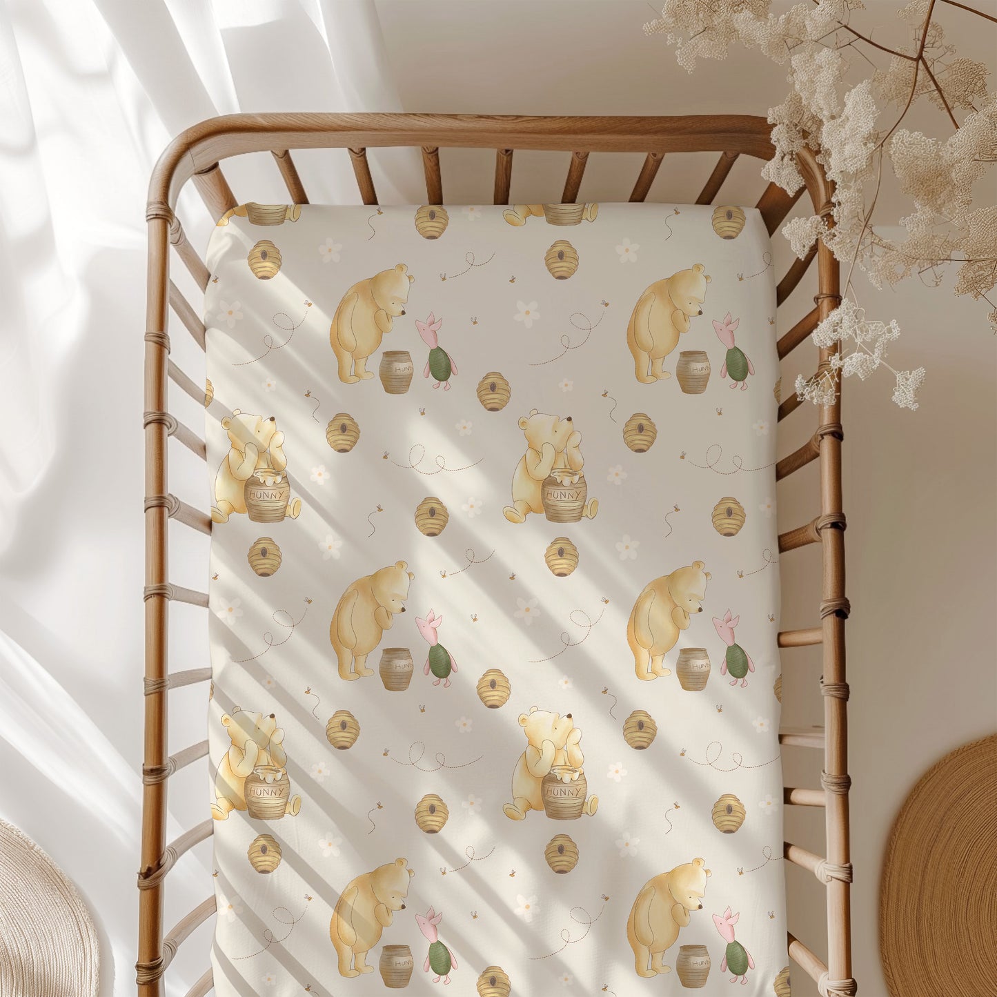 Crib with a patterned sheet featuring pooh bear, piglet, honey, bee hives and flowers in a softly lit room.