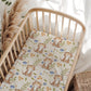 Crib with a patterned sheet featuring kittens and flowers, surrounded by decorative elements.