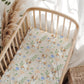 Crib with a patterned sheet featuring corgis and flowers, surrounded by decorative elements.