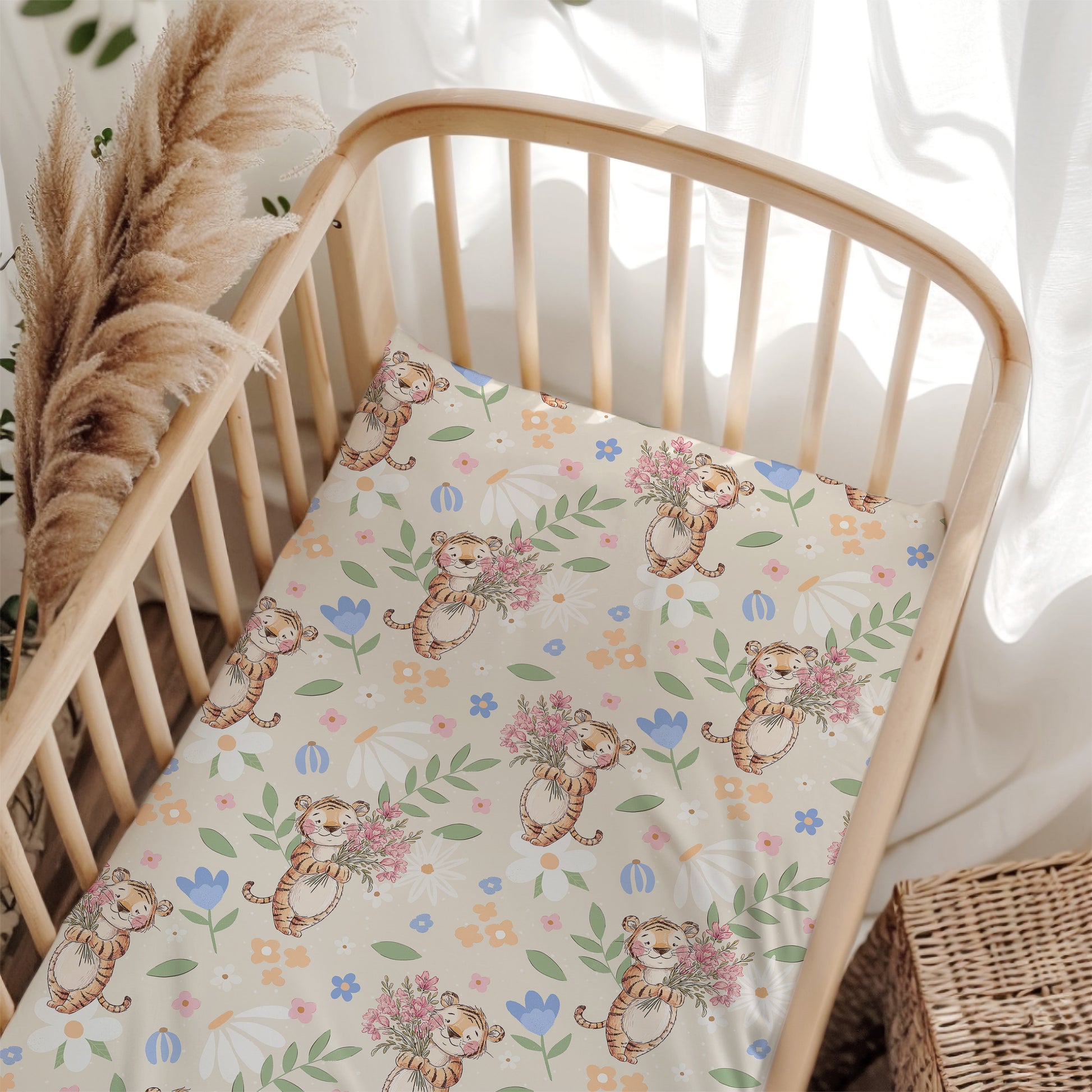 Crib with a decorative sheet featuring cartoon tigers and flowers, surrounded by pampas grass and white curtains.