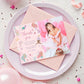 Pink birthday invitation with a photo of a girl in a white dress on a pink plate.